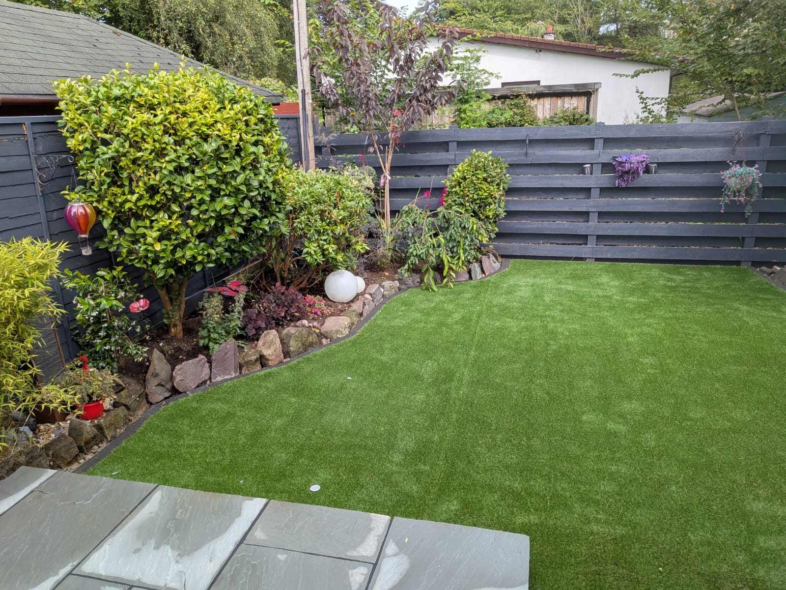 Curved artificial grass lawn with rockery border in a rear garden